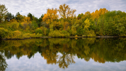 Forest autumn panoramic landscape - lakeside with trees with colorful leaves reflecting in calm water