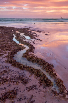 A colorful coastal sunset reflected in the water of an S shaped rock pool