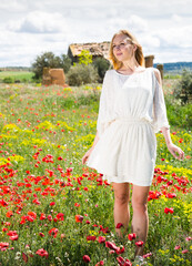 Young woman in white dress walking through a poppies plant outdoor