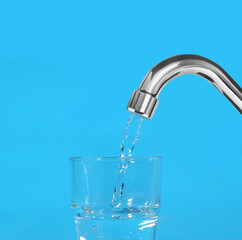 Filling glass with water from tap on light blue background