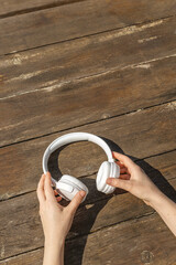 A girl holds white wireless headphones in her hands against the background of a wooden table