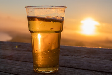 plastic cup with beer in the rays of the rising sun