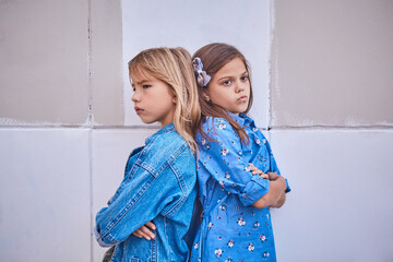 Cute two girl friends of 9 years old are standing together on the street, quarreling and sad. The concept of friendship, a quarrel.