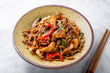 Plate of asian buckwheat soba noodles with vegetables, mushrooms and chicken on light gray background close up