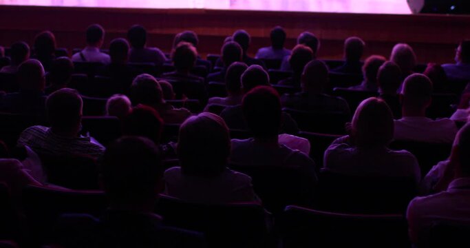 people at a conference or presentation, workshop, master class photograph. Back view. Staging in theatre. Many people in playhouse sitting in chairs and looking at scene. Full auditorium of people.