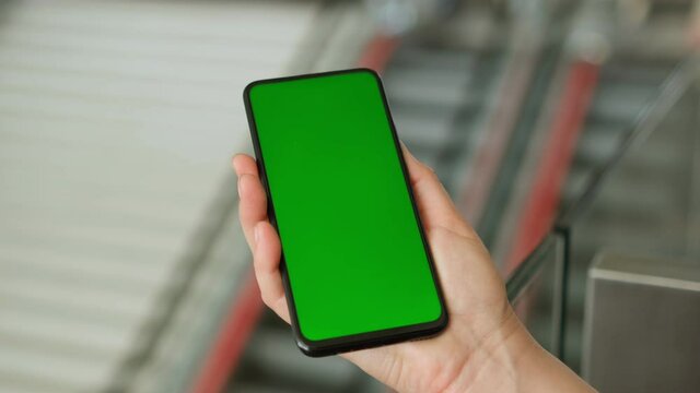 Back view of brunette holding chroma key green screen smartphone watching content. Shopping online. Shopping center. Department store. Mall. Gadgets and contemporary people concept.