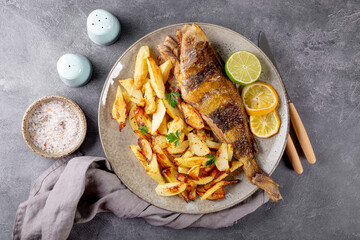 Baked sea bass or lingcod fish with potatoes on a plate and gray background top view