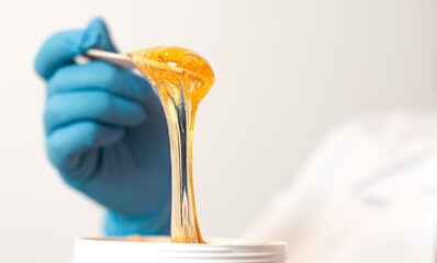 Hands hold a spatula and a jar of sugar paste for sugaring on a light background
