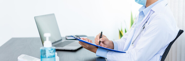 Medical concept a male doctor wearing a mask writing prescription to patient at his modern clinic...