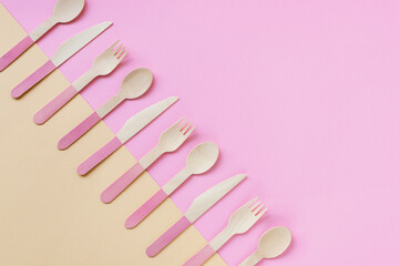 Disposable bamboo spoons, forks and knives on yellow and pink background. Zero waste concept. Top view, copy space