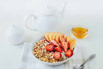 breakfast porridge oatmeal with cereal granola strawberries peaches honey in a white plate on the background of a white teapot and bowls with honey on a white plate