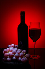 Fototapeta premium Wine bottle glass and bunch of grapes on dark background
