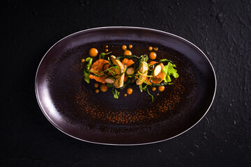 dish with salmon tartare, croutons, sauted courgettes and caper flowers. dark background, top view