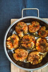 Potatoes baked with rosemary and spices in a frying pan, on a wooden chopping board, blue linen table cloth, top view vertical image