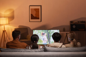 Back view of young people watching movies at home while sitting on sofa, focus on TV screen, copy...