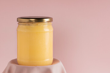 Ghee or clarified butter in jar on pink background. Minimal style. Scene with geometric shapes. Copy space.