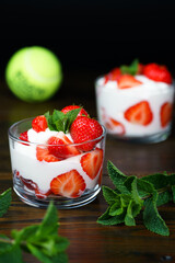 Whipped cream and strawberries served in a glass. Dark wooden table, tennis ball in bokeh, high...