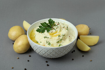 Bowl of mashed potatoes and ingredients on gray background