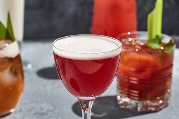 Red Martini Sour Cocktail is a martini based cocktail topped with egg white. Vintage table with sunshine and shadow. Breakfast alcohol drink with martini and lemon juice.
