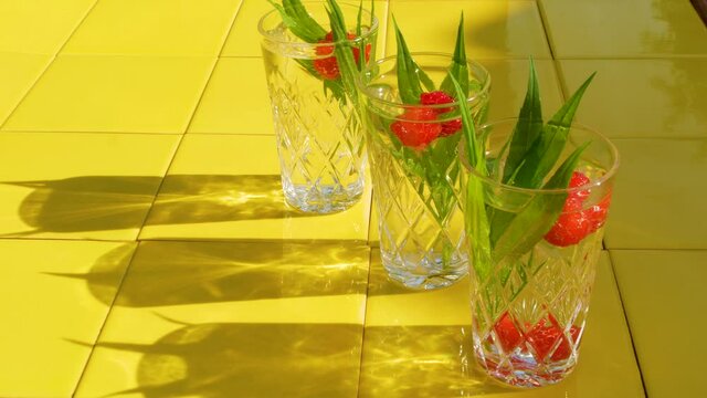 Refreshing summer drinks in crystal glasses with green leaves raspberry yellow tile background shadows. Sweet cold natural cocktail hot summer day. Soda water fruits berries mint tonic. Party vacation