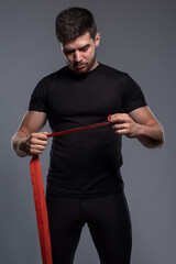 Young man with red boxing tape in hands on grey background