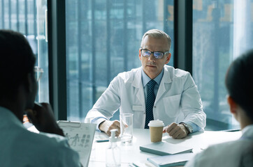 Portrait of white haired senior doctor presiding at medical meeting in conference room, copy space