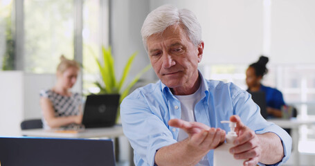 Mature businessman washing hands with antiseptic gel before working on computer in office