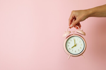 Female hand holds alarm clock on pink background