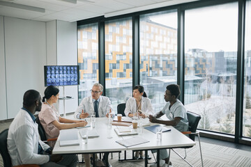 Wide angle view at doctors sitting at meeting table in conference room during medical council, copy space