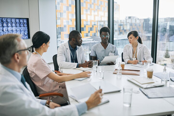Large group of doctors discussing case while sitting at meeting table during medical conference, copy space