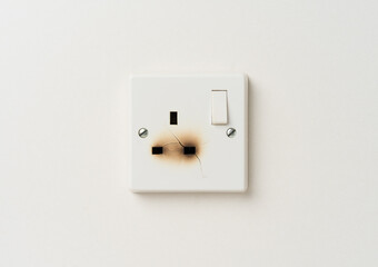 Broken electrical domestic power socket with cracks and burn marks on a white wall - obrazy, fototapety, plakaty