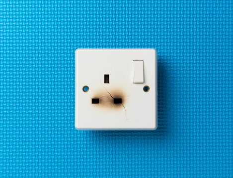 Damaged electrical wall power socket with burn marks and cracks on a blue background