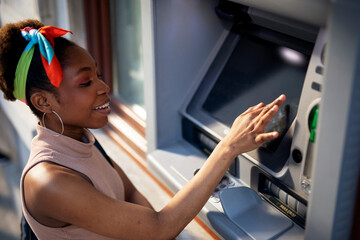 Beautiful african women using ATM machine. Attractive young woman withdrawing money from credit card at ATM.