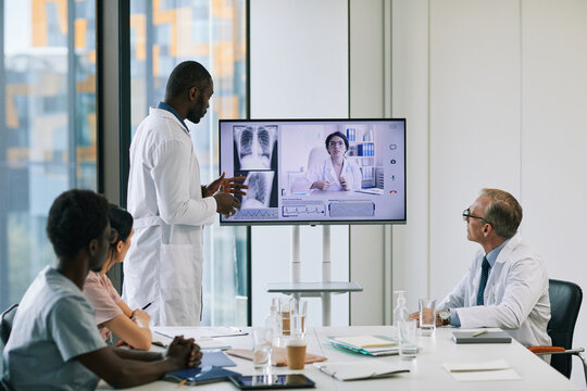 Portrait Of African-American Doctor Standing By Digital Screen In Onference Room And Talking To Expert Via Video Call, Copy Space