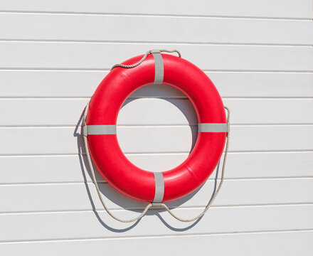 Red lifebuoy ring hanging on white wooden wall