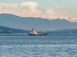 Fuel tanker or bunker ship sailing on water at mountains background