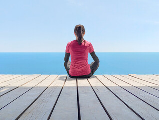 Fototapeta na wymiar Back view of woman sitting on wooden floor and meditating at blue sea background at sunny day