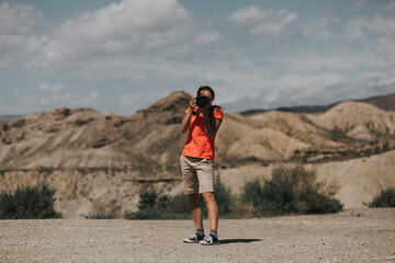 Sports woman photographer taking photos in Tabernas Desert, Spain, in a sunny day, with an orange color t-shirt.