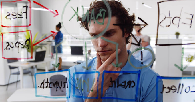 Young pensive man looking at data on glass board in modern office