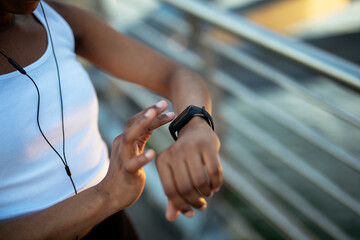 Young african woman training outdoors. Female runner using smart watch.