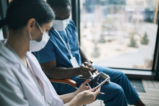 Side View Portrait Of Two Doctors Wearing Masks While Looking At Digital Tablet