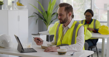Foreman in reflective vest having video chat while eating lunch in canteen