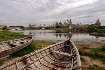 Fototapeta na wymiar View of old wooden boats on the shore of the White Sea Bay and the Solovetsky Monastery in the background on a cloudy summer day, Solovetsky Island, Arkhangelsk region, Russia