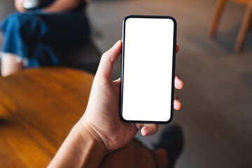 Mockup image of a man holding black mobile phone with blank white screen in cafe