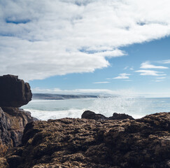 the rocky shore of the ocean and white waves leave sparkling traces in the water, the horizon is visible in the distance.