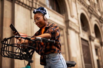 Fototapeta na wymiar Happy young woman riding bicycle in the city. Beautiful african woman using the phone outdoors..
