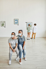Wide angle view at African-American boy and girl looking at paintings in art gallery and wearing...