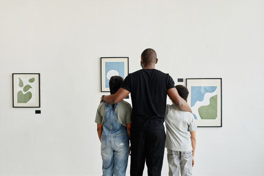 Minimal back view at African-American family looking at paintings in modern art gallery, copy space