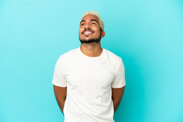 Young Colombian handsome man isolated on blue background thinking an idea while looking up