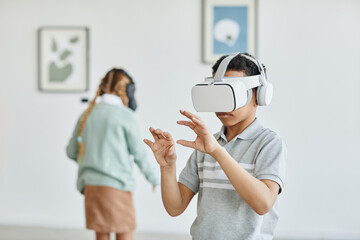 Waist up portrait of schoolboy wearing VR headset in art gallery while enjoying immersive...